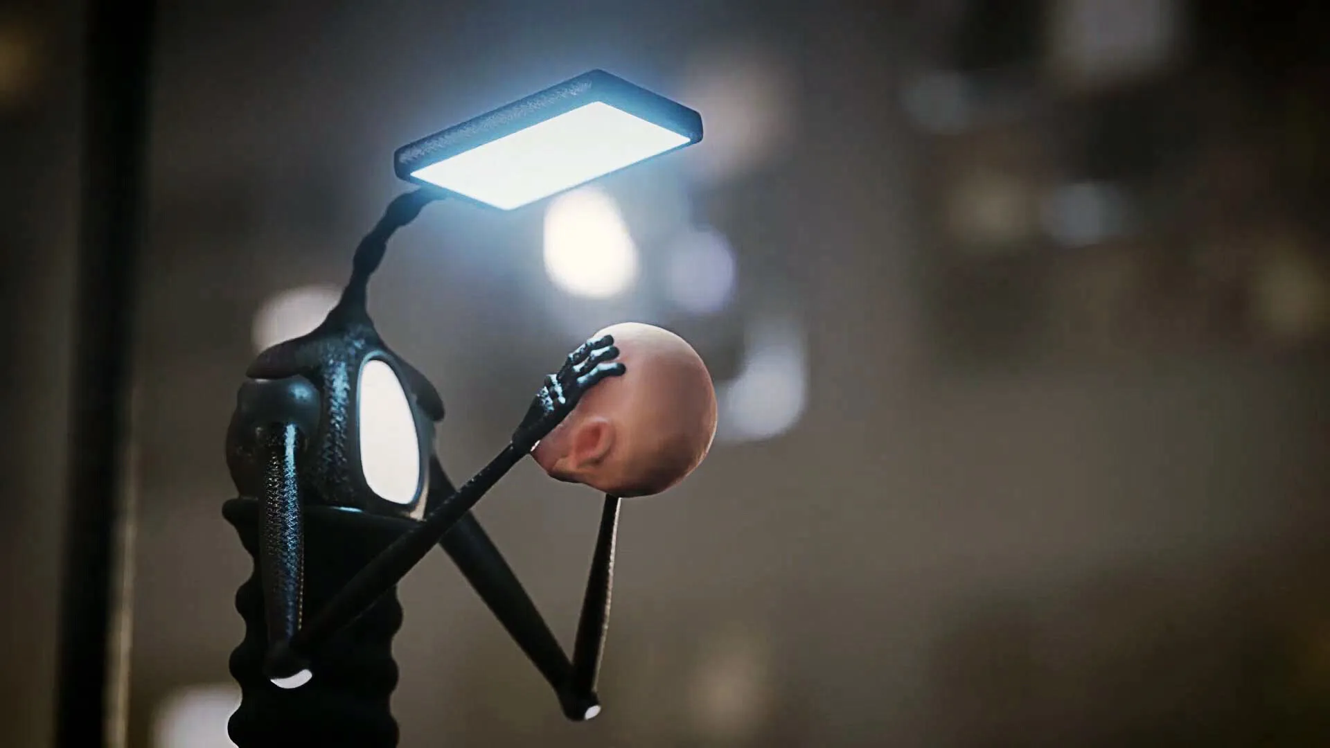 A robot holding a human head under a floodlight, blurred city behind