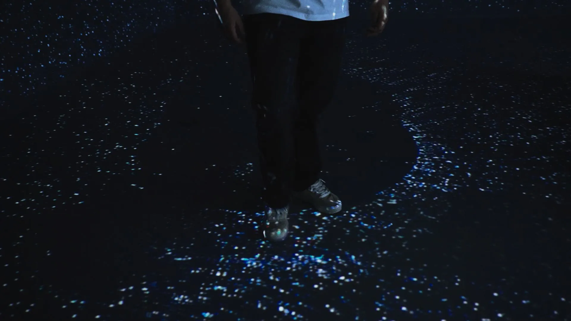 A visitor walking across a dark floor scattered with fine white and blue particles
