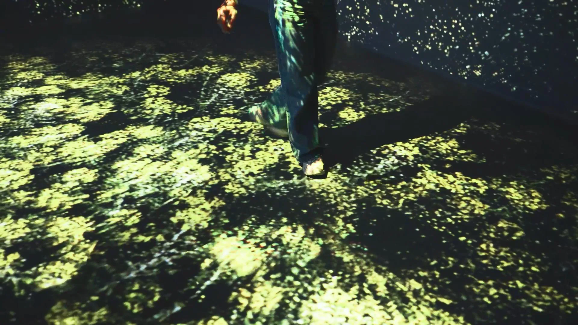 A visitor's legs on a floor of yellow-green foliage particles