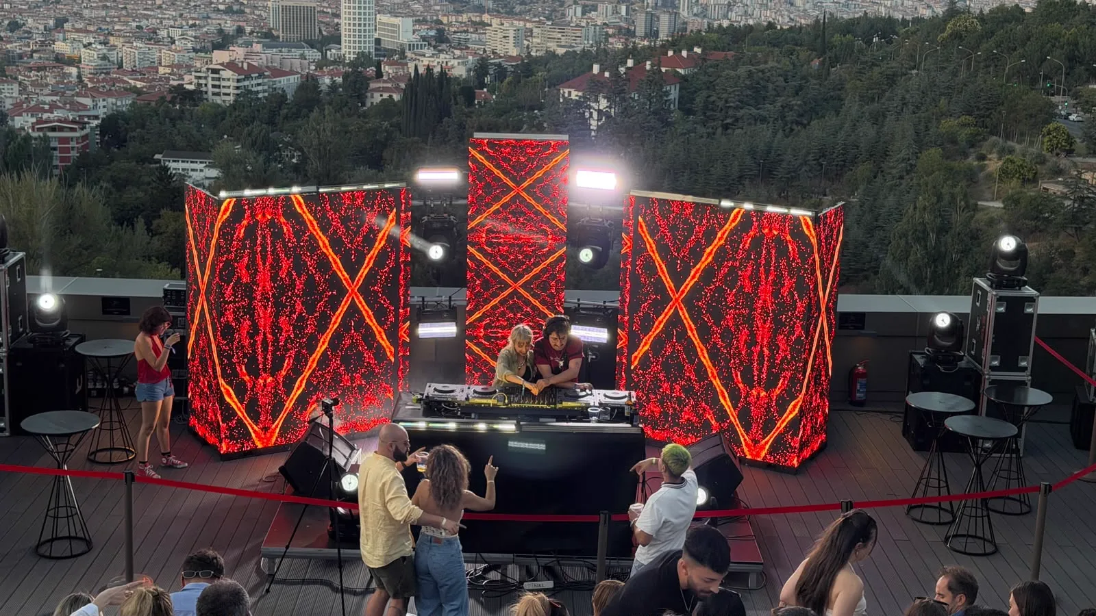 The stage at sunset: a red lattice across the screens, the DJ between them, Ankara behind