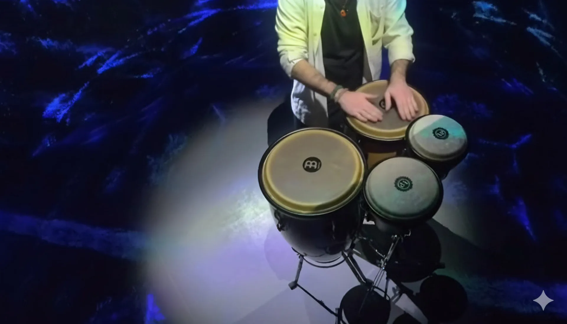 The percussionist from above, hands on the congas, the floor around him lit blue