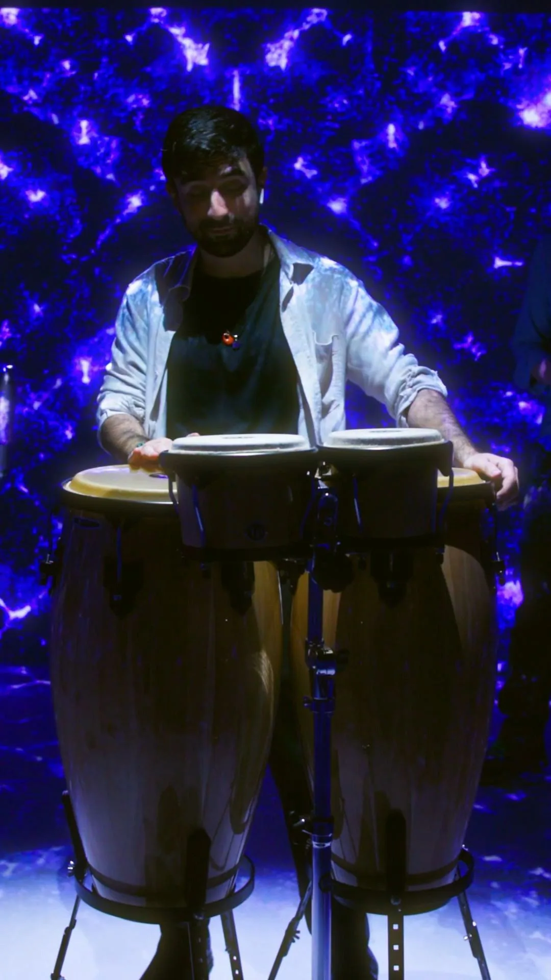The percussionist in a white shirt against a wall of violet cymatic pattern