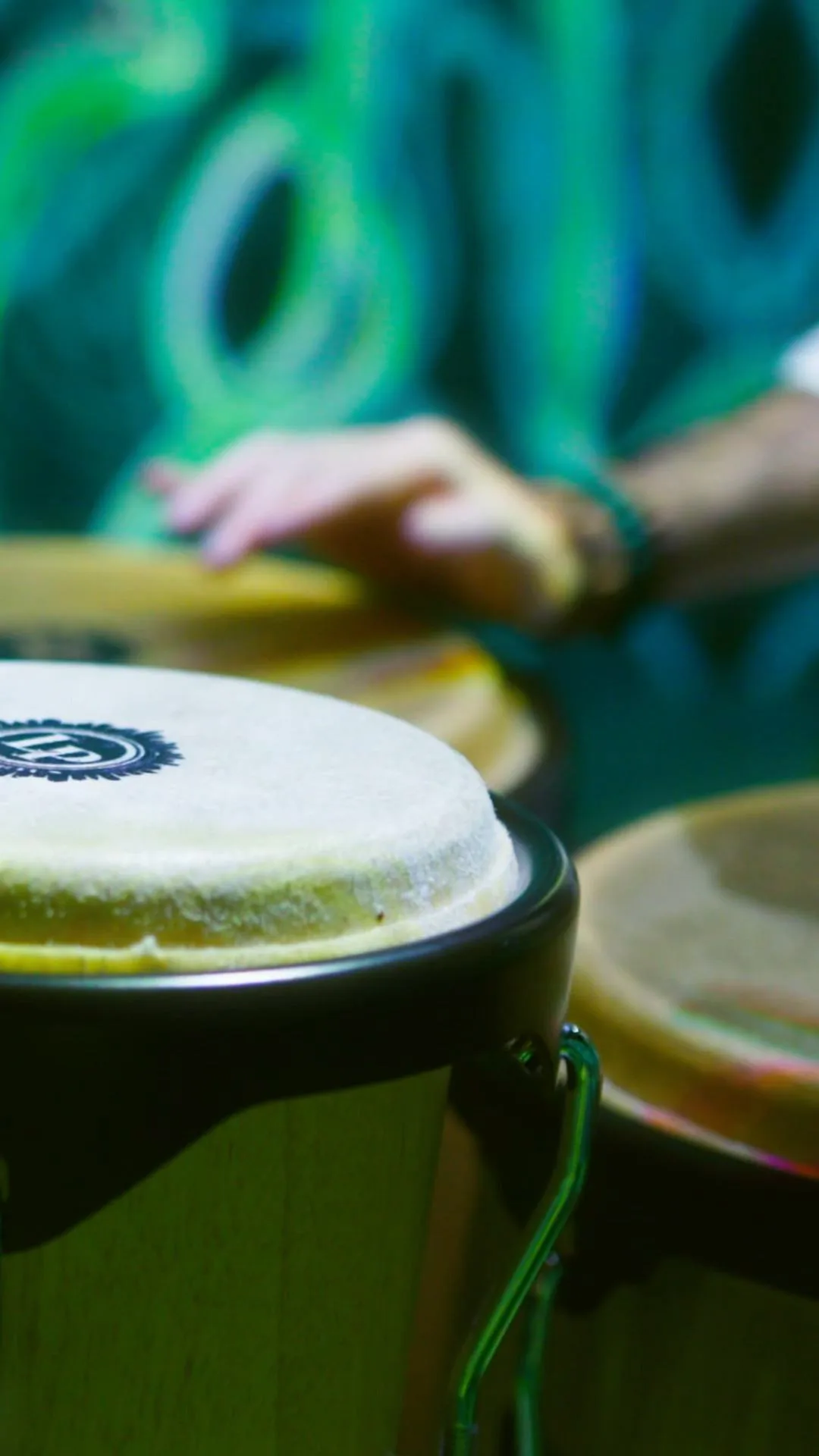 Hands striking a conga, the pattern blurred green behind
