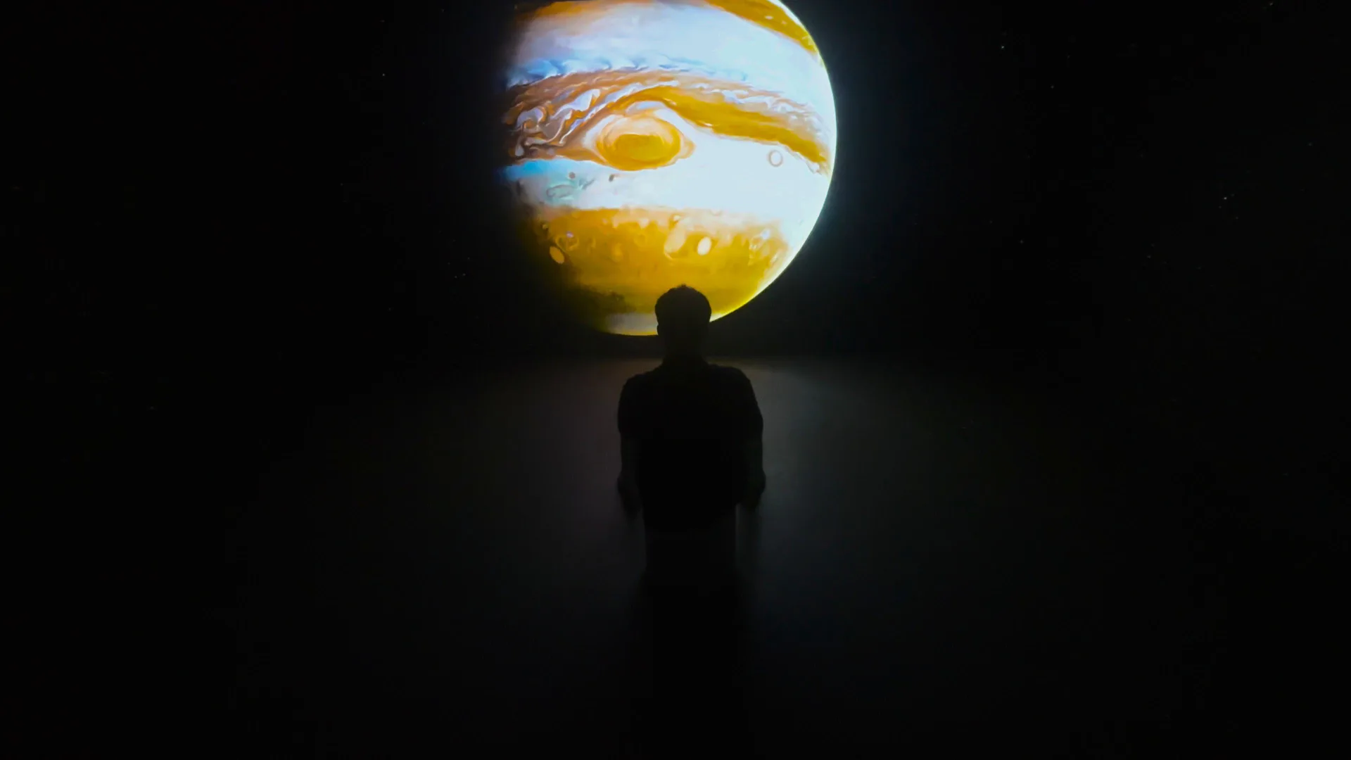 A single visitor in silhouette before Jupiter on the far wall